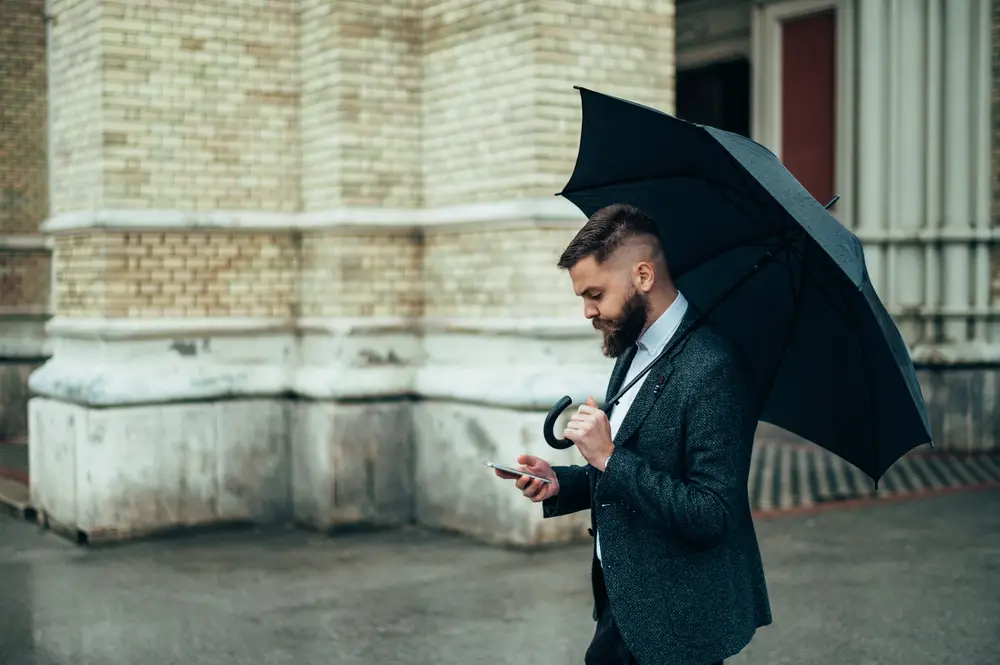 Fashion man using a smartphone and holding a black rain umbrella