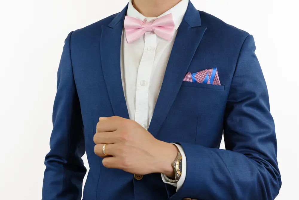 Man in blue suit with pink bow tie, flower brooch, and pink blue stripe pocket square