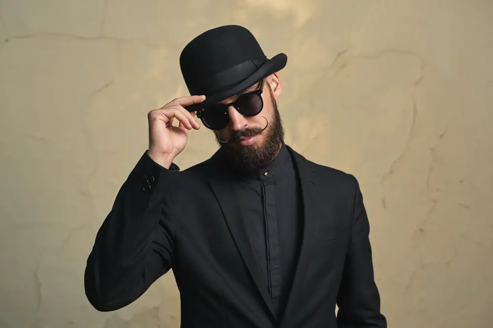 Man wearing black suit and shirt and a black Derby Hat