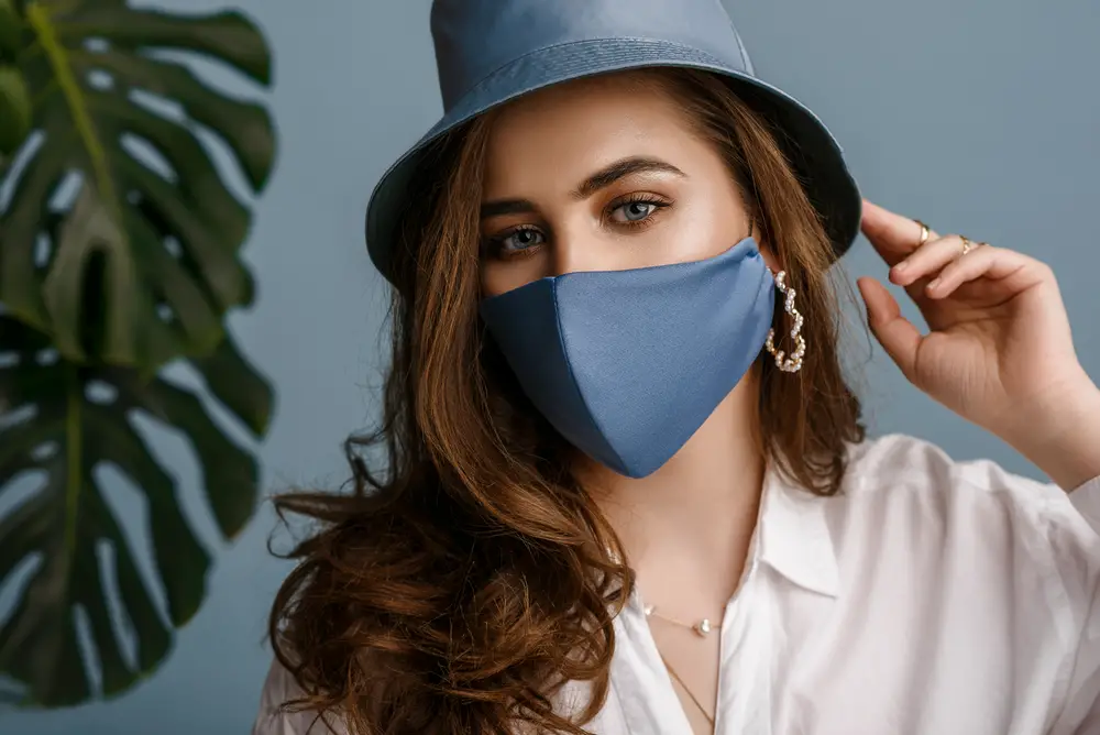 Woman wearing stylish outfit with luxury designer protective blue face mask, bucket hat, pearl earrings