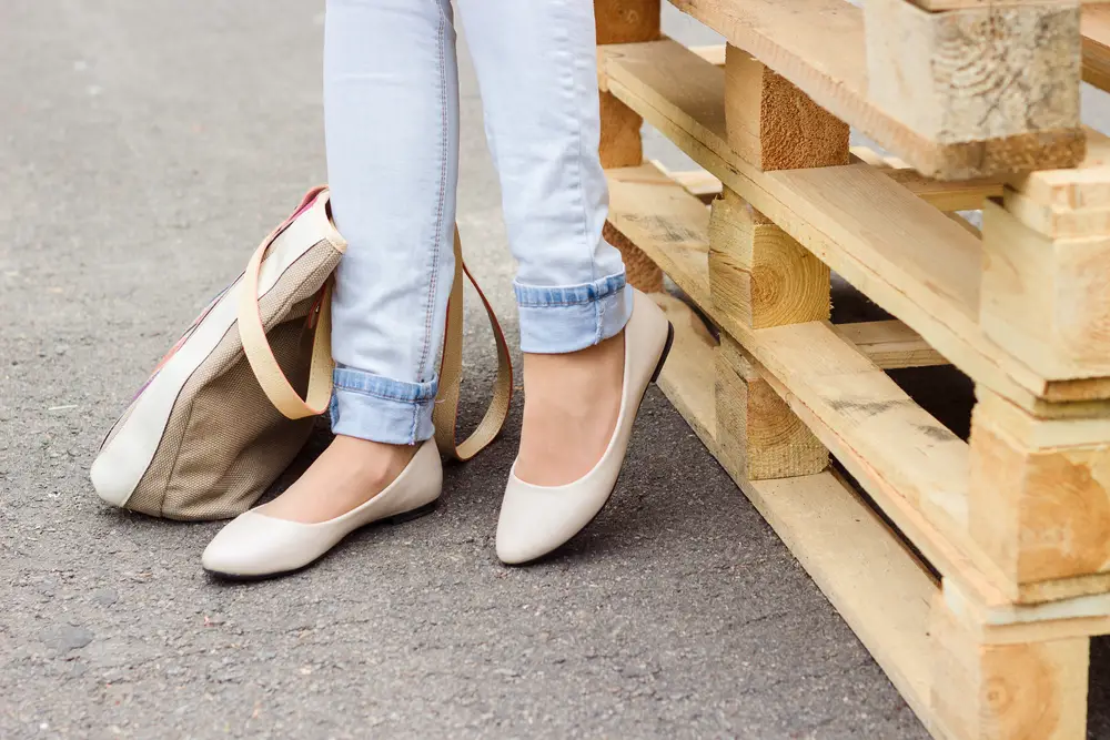 Woman's legs in blue jeans and white ballet flat shoes with beige bag