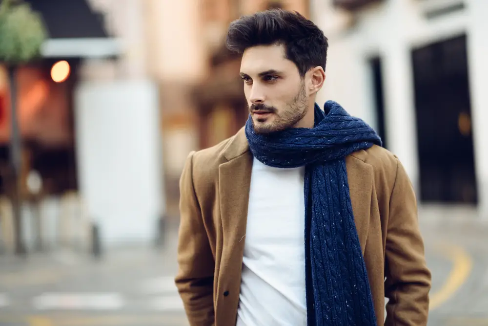 Young bearded guy with modern hairstyle with coat, scarf, blue jeans and t-shirt