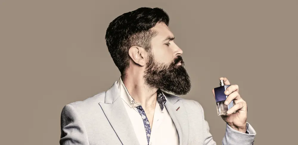 cologne bottle and perfumery, cosmetics, scent cologne bottle, male holding cologne. Masculine perfume, bearded man in a suit.