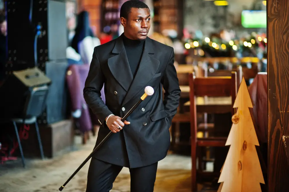gentleman in elegant black jacket, holding retro walking stick as cane flask or tippling cane with golden diamond ball handle
