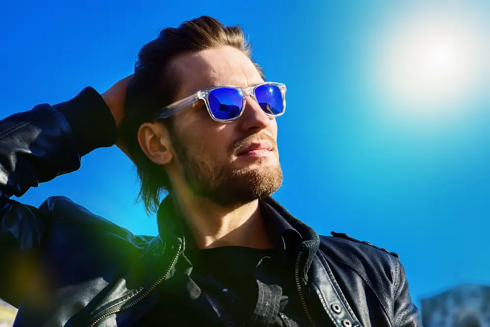 man in sunglasses and leather jacket over blue sky. Men's beauty, fashion