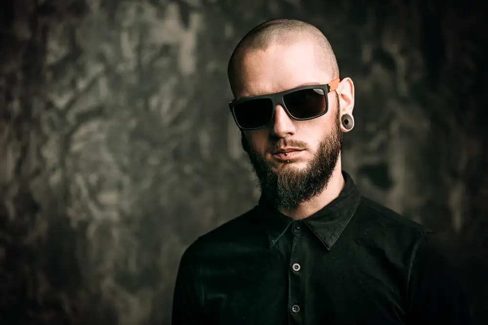man wearing sunglasses and black t-shirt with piercing in the ears and lips