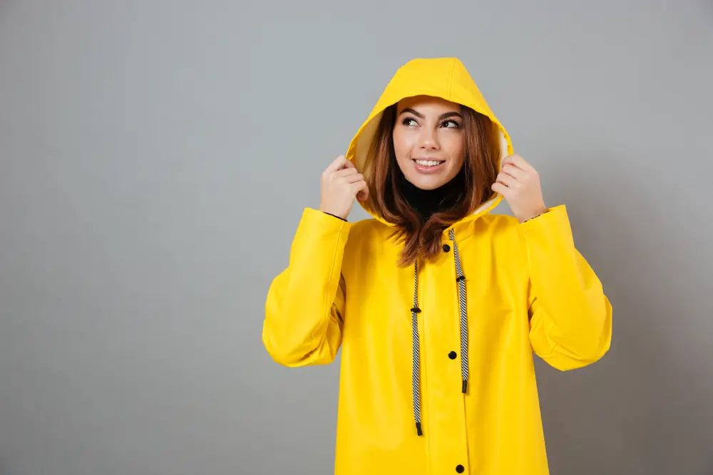 smiling girl dressed in raincoat posing with hood on her head