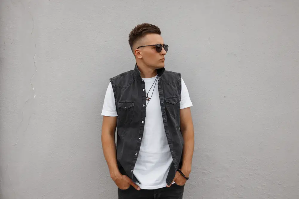 young man hipster in a vintage denim vest in a white T-shirt in jeans in sunglasses