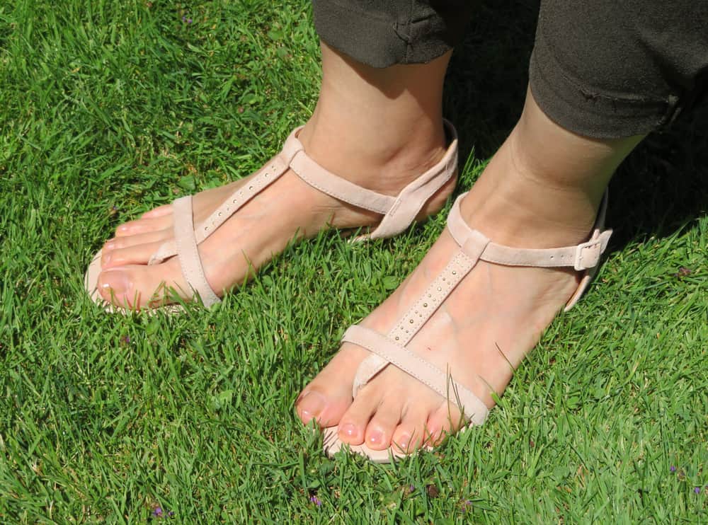  woman feet in t strap sandals standing on green grass