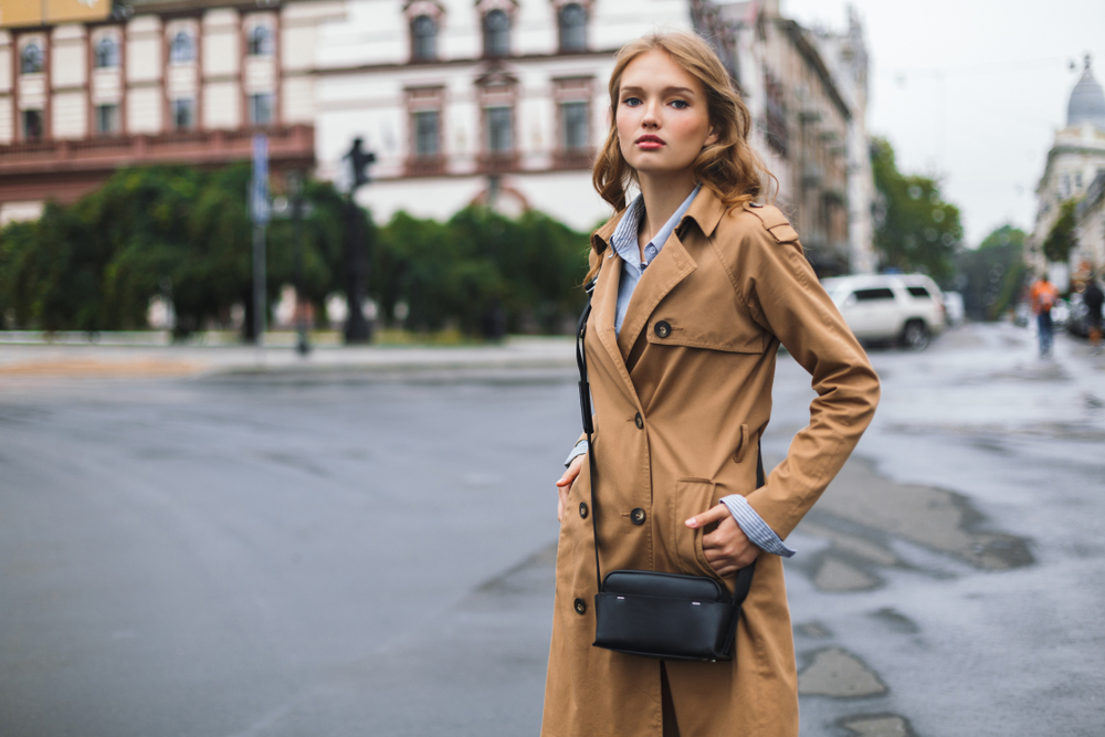 woman in trench coat with little black cross bag 