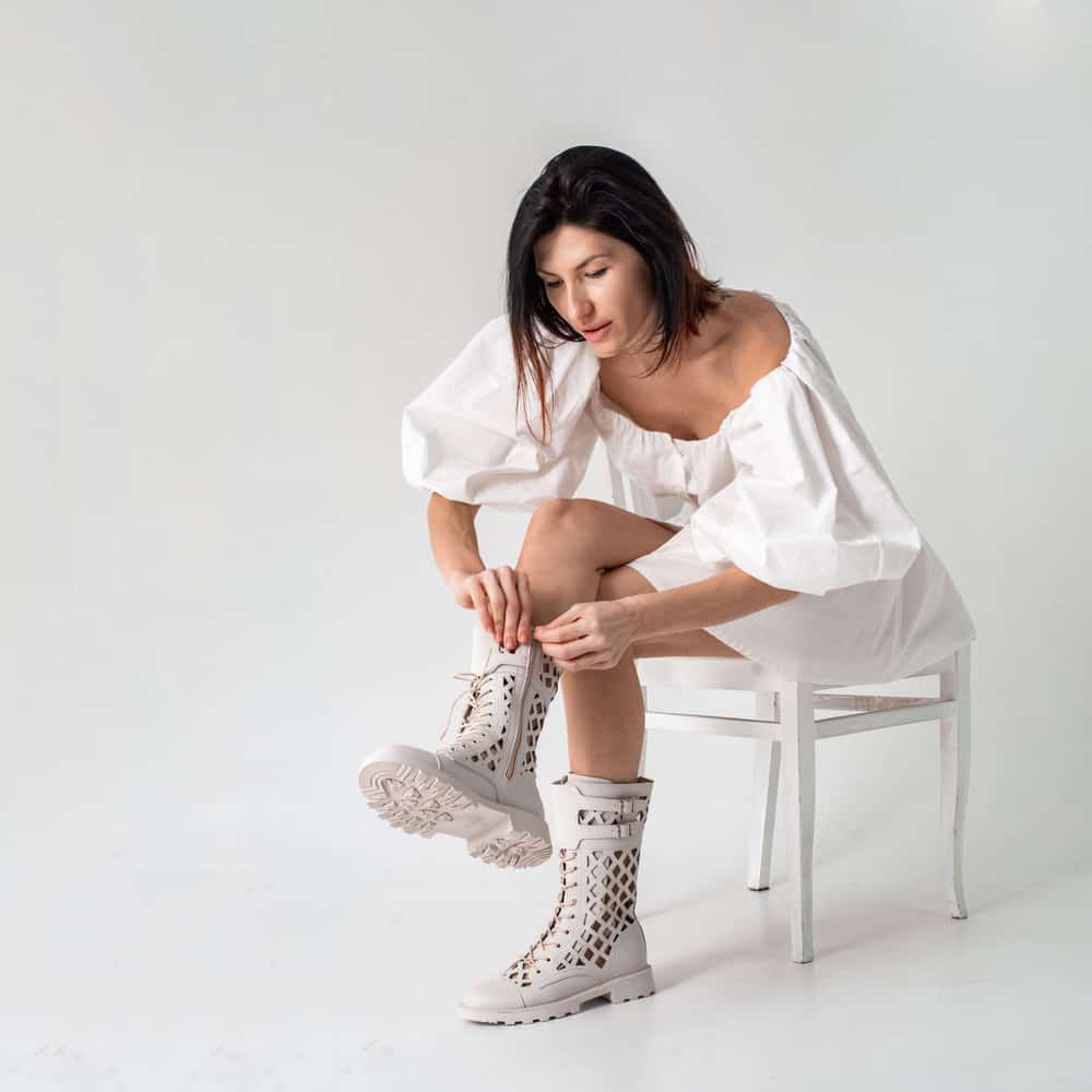 woman in white dress puts on white summer perforated military lace-up boots 