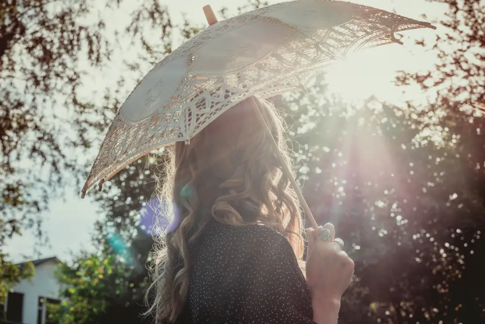 young woman hiding from the sun under white lace parasol umbrella